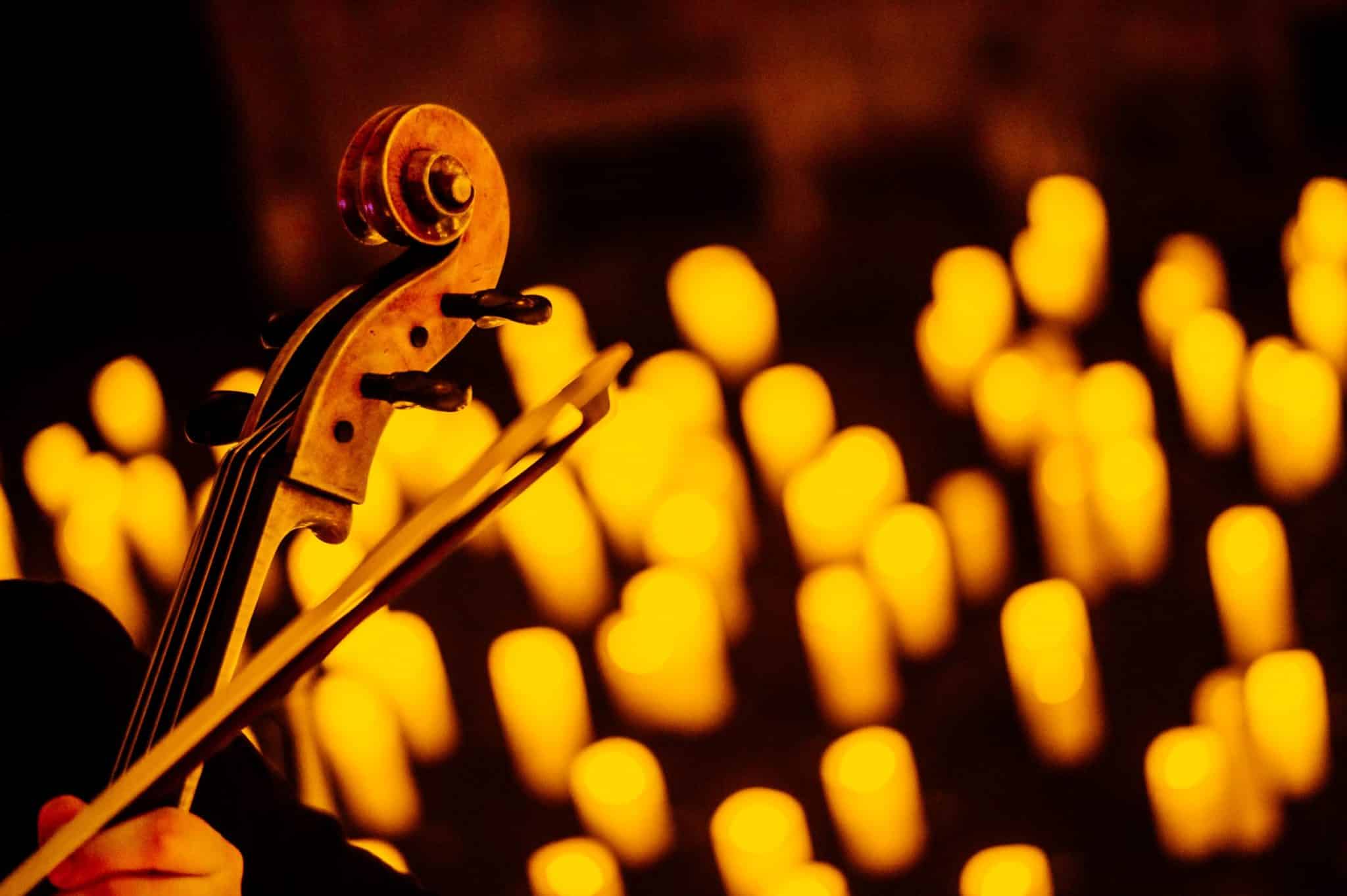 The top of a string instrument and bow is visible with the blurry image of candles in the background at a Candlelight concert.