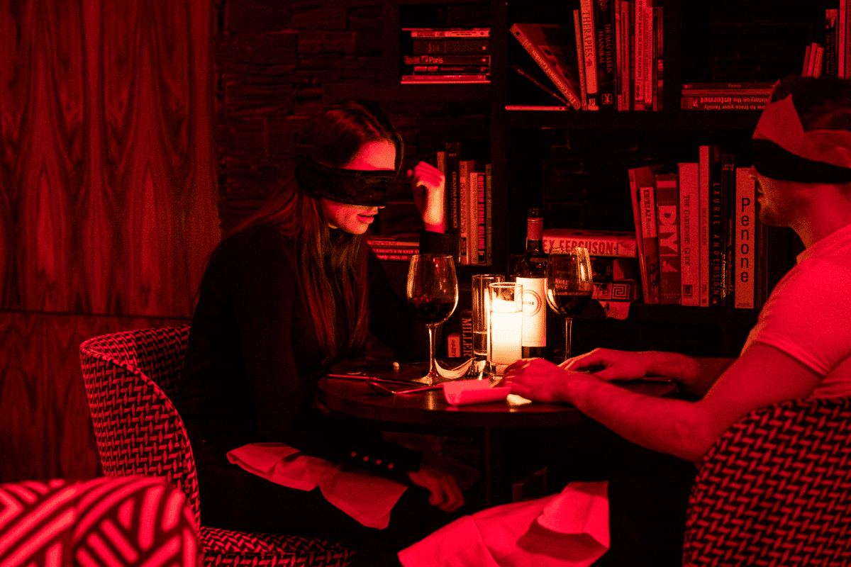 A couple sitting at a table blindfolded at the Dining in the Dark experience.