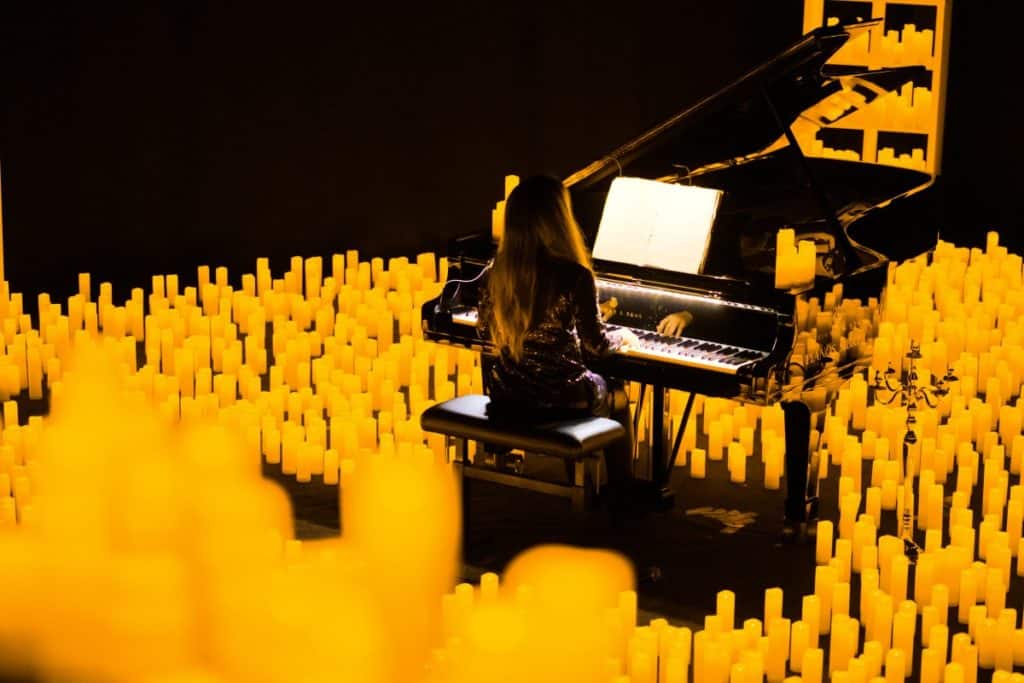 A back shot of a musician playing the grand piano amid a sea of candles