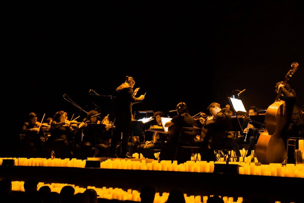 A conductor conducting a Candlelight orchestra on a stage surrounded by candles.