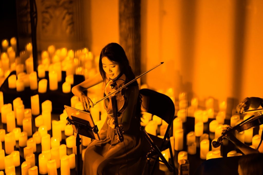 A musician playing the violin amid a sea of candles