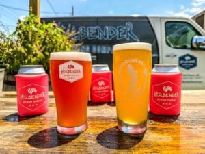 Pale and blonde beers in front of a van that reads 'Hellbender Brewing Company'.