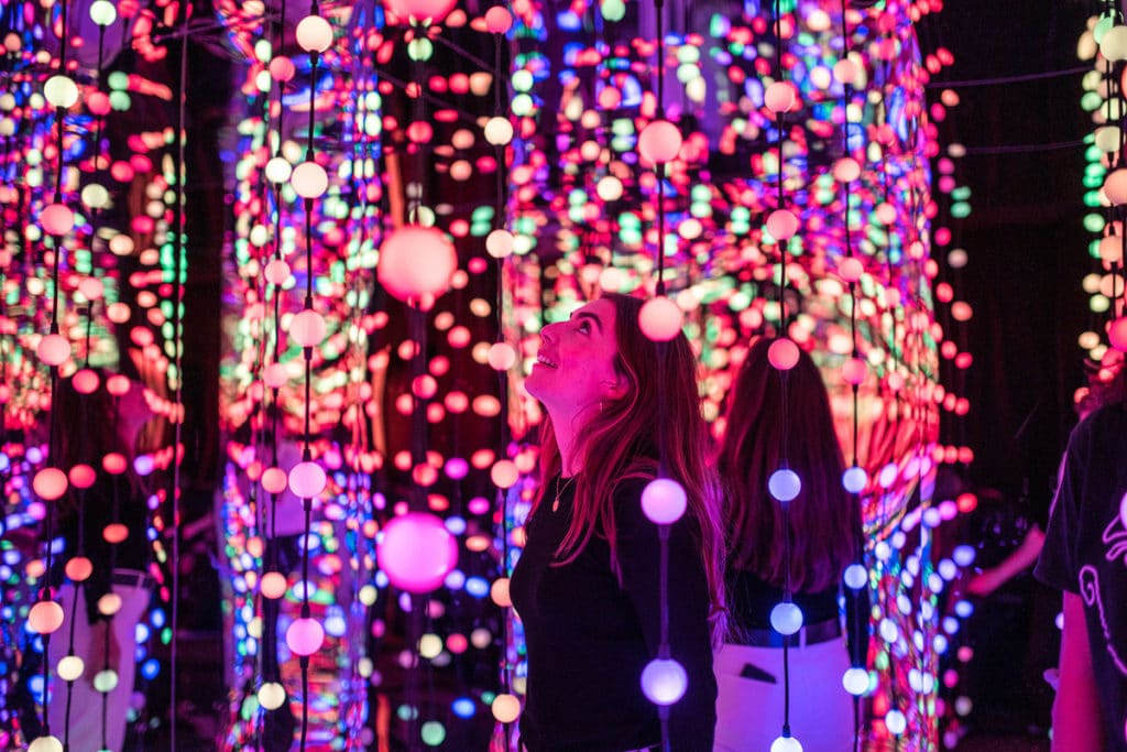 girl standing among thousands of colorful lights
